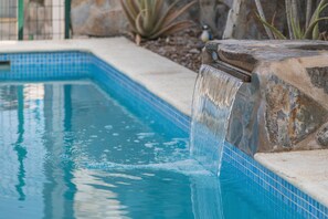 Ein Schwimmbecken mit Wasserfall, umgeben von Stein und Fliesen.
