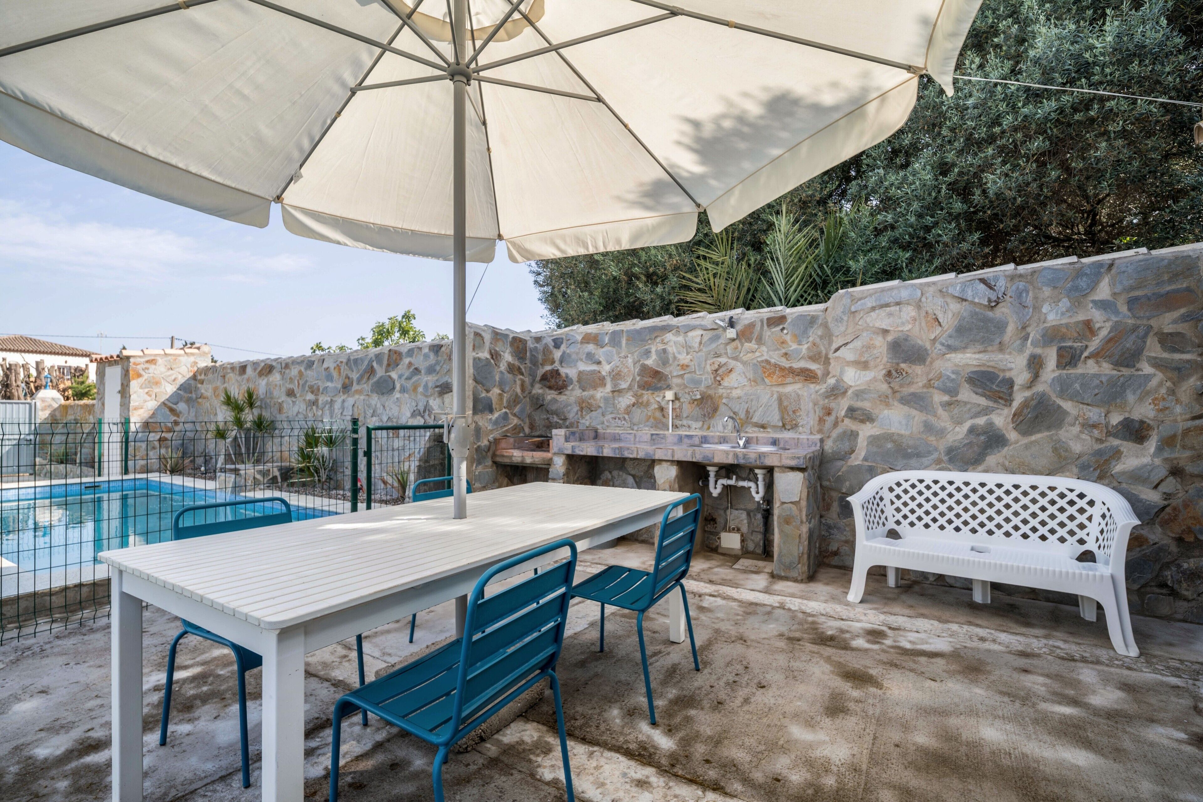 Une terrasse avec une piscine, un mur en pierre, une table d’extérieur, des chaises et un banc blanc.