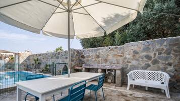 Une terrasse avec une piscine, un mur en pierre, une table d’extérieur, des chaises et un banc blanc.