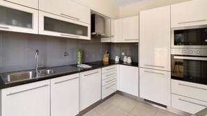 Una cocina moderna con armarios blancos, encimera negra, electrodomésticos de acero inoxidable y una campana extractora visible.