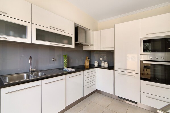 A modern kitchen with white cabinets, a black countertop, stainless steel appliances, and a visible ventilation hood.