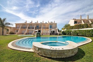 Piscina com deck de pedra, um edifício grande com várias varandas e um gramado bem cuidado.
