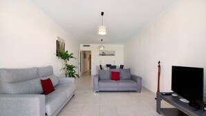 Una sala moderna con dos sofás grises, un televisor de pantalla plana y un área de comedor al fondo.