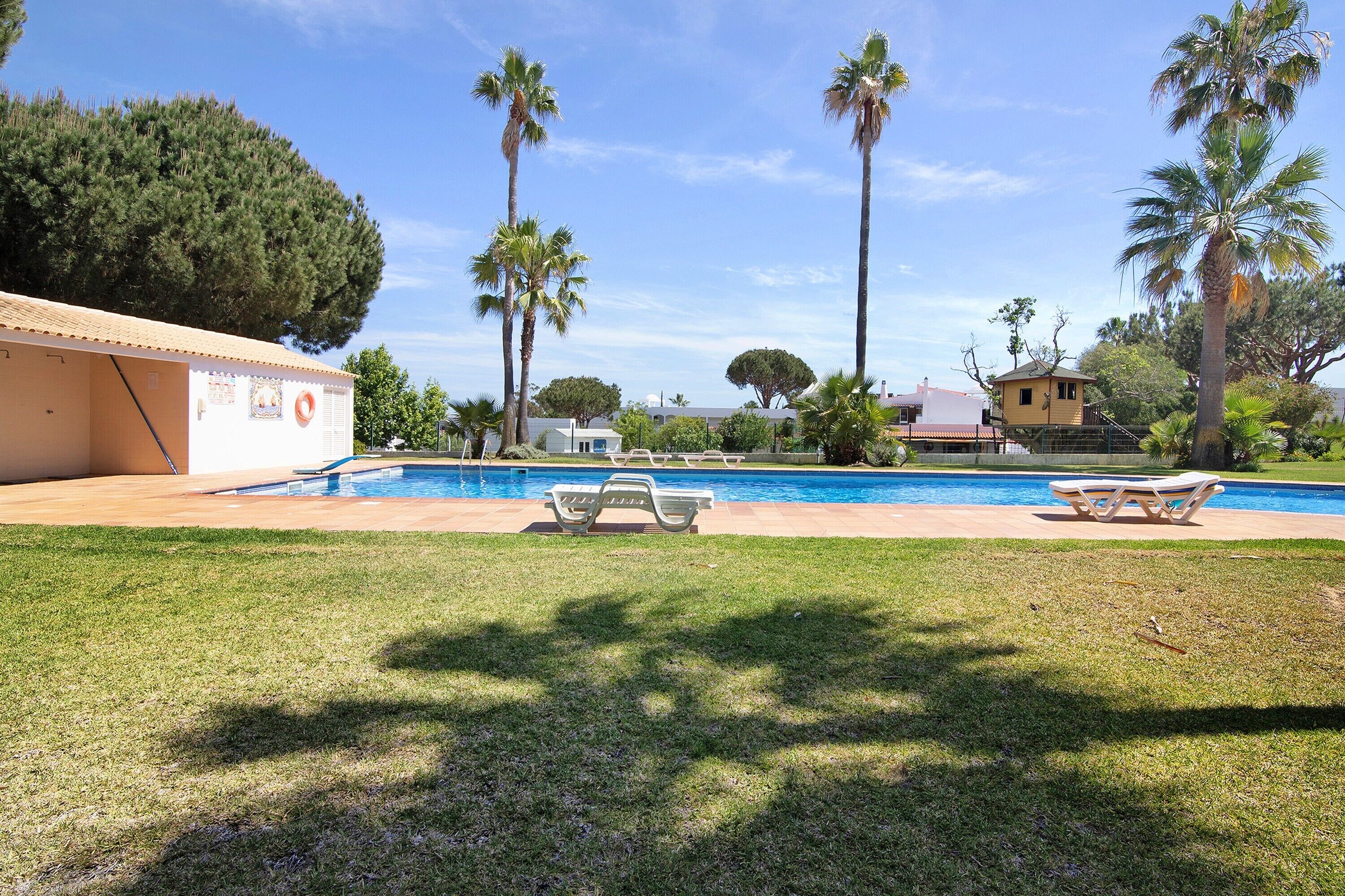 A swimming pool with lounge chairs, palm trees, and a building with a tiled roof.