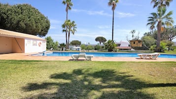 A swimming pool with lounge chairs, palm trees, and a building with a tiled roof.