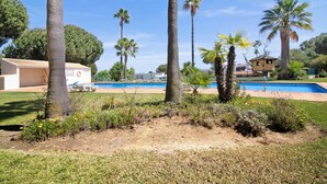 A pool area with palm trees, a small building, and a house in the background. - Apartment 'Yara Beach Apartments with Terrace' with Shared Pool, Wi-Fi and Air Conditioning (Albufeira)