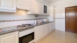 A kitchen with white cabinets, a gas stove, a microwave, and a wooden door. - Apartment 'Yara Beach Apartments with Terrace' with Shared Pool, Wi-Fi and Air Conditioning (Albufeira)