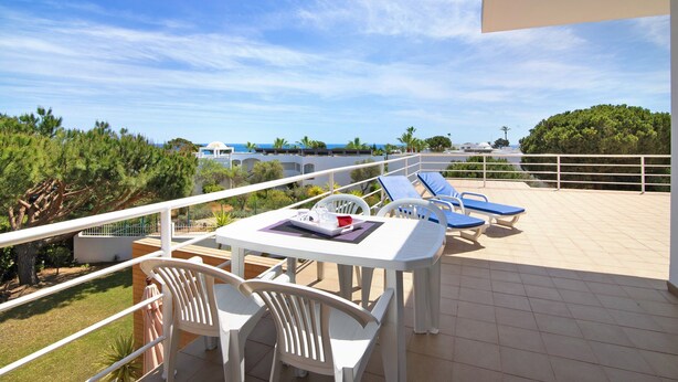 A terrace with a table and chairs, a pool area with lounge chairs, and a view of the sea and greenery. - Apartment 'Yara Beach Apartments with Terrace' with Shared Pool, Wi-Fi and Air Conditioning (Albufeira)