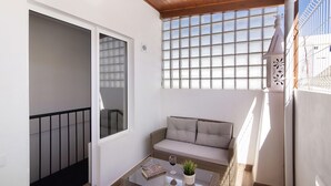 Un balcón con sofá, una mesa de centro de vidrio, una planta en maceta y un libro.