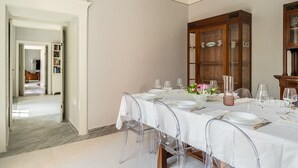 Een eetkamer met een lange tafel voor zes personen, transparante stoelen en een houten kast met glazen deuren.