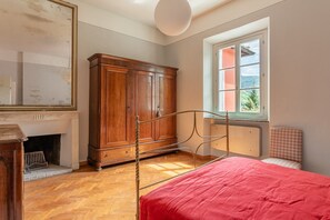 Een slaapkamer met een bed, een houten garderobe, een open haard en een raam met uitzicht.