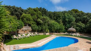 A swimming pool with a curved edge, surrounded by a pebble border and a stone wall. There are lounge chairs aligned along the pool's edge. - Country House 'Son Favar Capdepera' with Private Pool, Private Terrace and Wi-Fi (Capdepera)