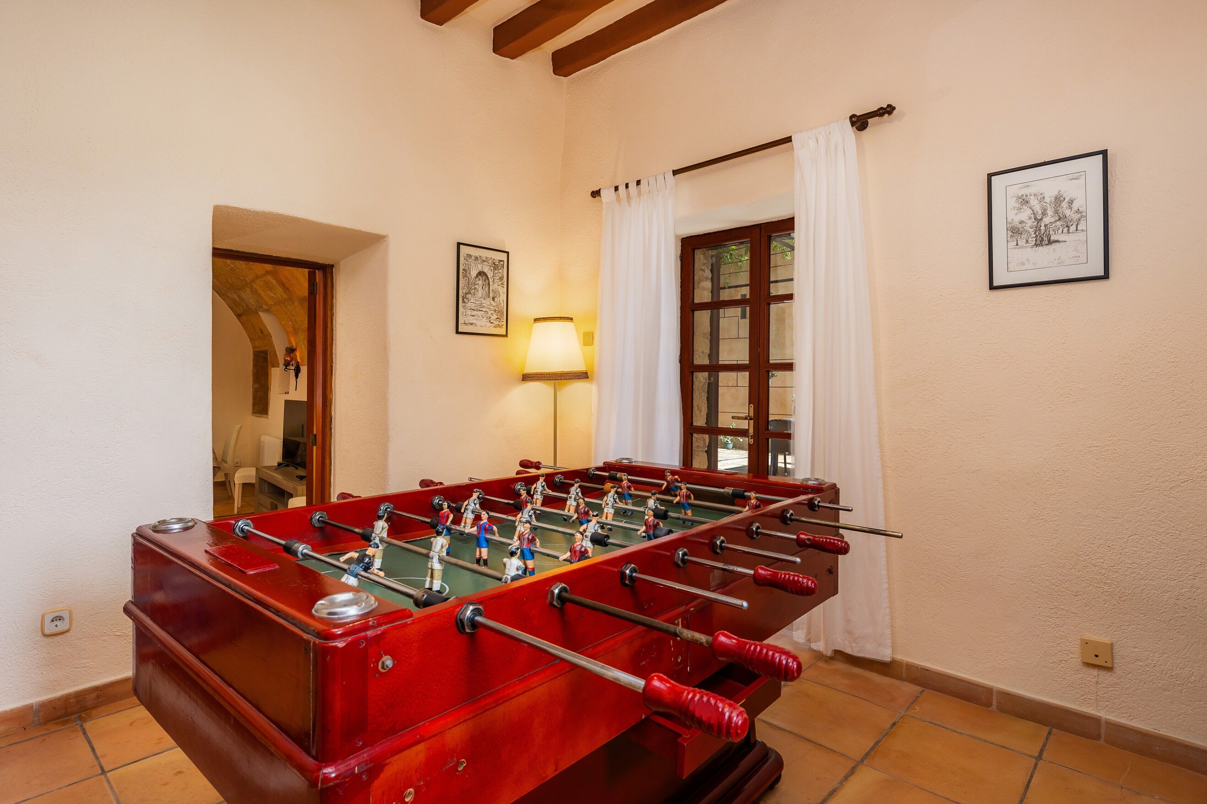 A red foosball table in a room with white walls, a lamp, and framed pictures.