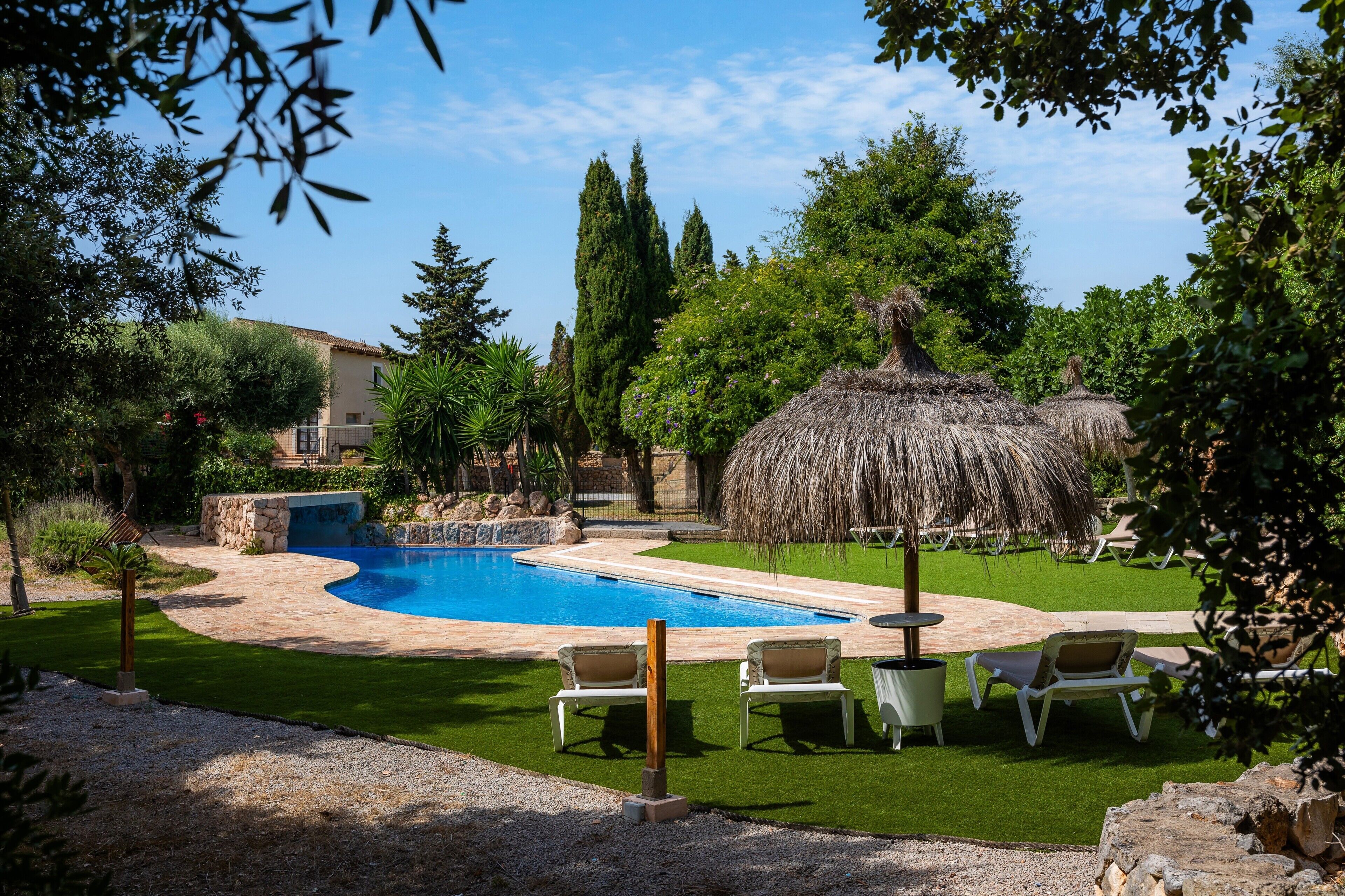 A swimming pool surrounded by grass, trees, and lounge chairs.