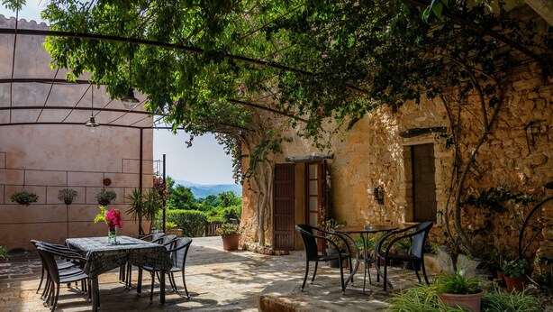 An outdoor patio with stone flooring, metal chairs, a table with a vase of flowers, and potted plants. - Country House 'Son Favar Capdepera' with Private Pool, Private Terrace and Wi-Fi (Capdepera)