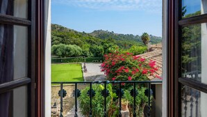 A balcony with a view of a green lawn, a flower bed with pink flowers, and a hilly landscape in the distance. - Country House 'Son Favar Capdepera' with Private Pool, Private Terrace and Wi-Fi (Capdepera)