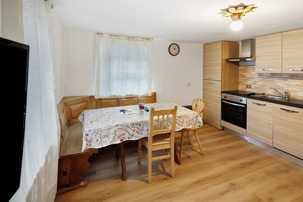 Une cuisine de taille réduite avec des meubles en bois, une table à manger avec des chaises, une horloge au mur et un luminaire moderne.