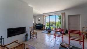 A spacious living area with a piano, multiple chairs, a large window with curtains, and a view of greenery. - Villa 'Les Terrasses De Gordes' with Private Pool, Private Terrace and Wi-Fi (Gordes)