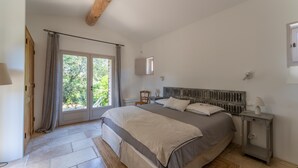 A bedroom with a bed, a nightstand, a window with curtains, and a wooden ceiling beam. - Villa 'Les Terrasses De Gordes' with Private Pool, Private Terrace and Wi-Fi (Gordes)