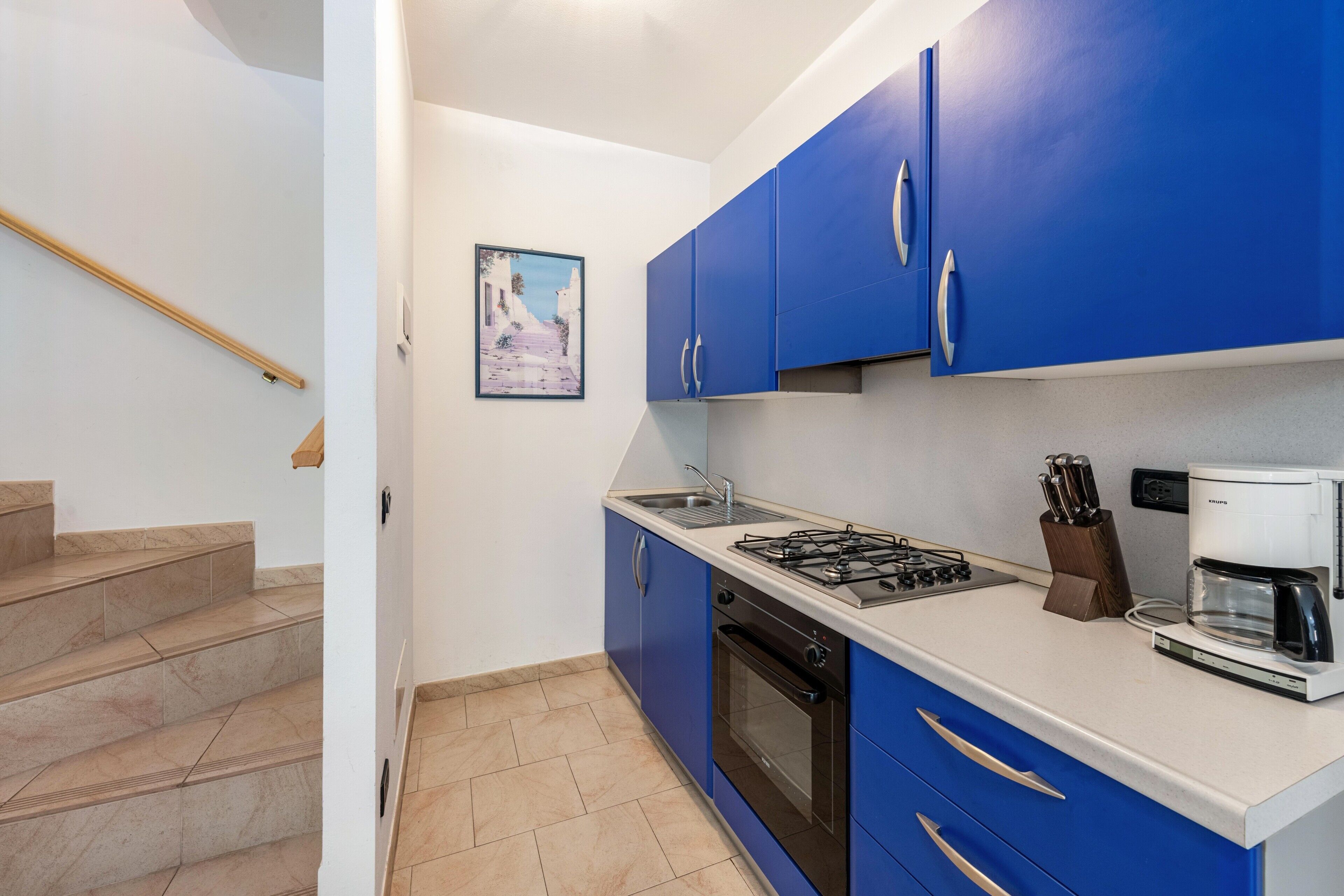 A kitchen with blue cabinets, a gas stove, an oven, a coffee maker, and a sink.
