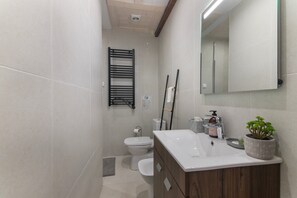 Een moderne badkamer met een wit wastafelmeubel, een spiegel, een handdoekrek en een toilet.
