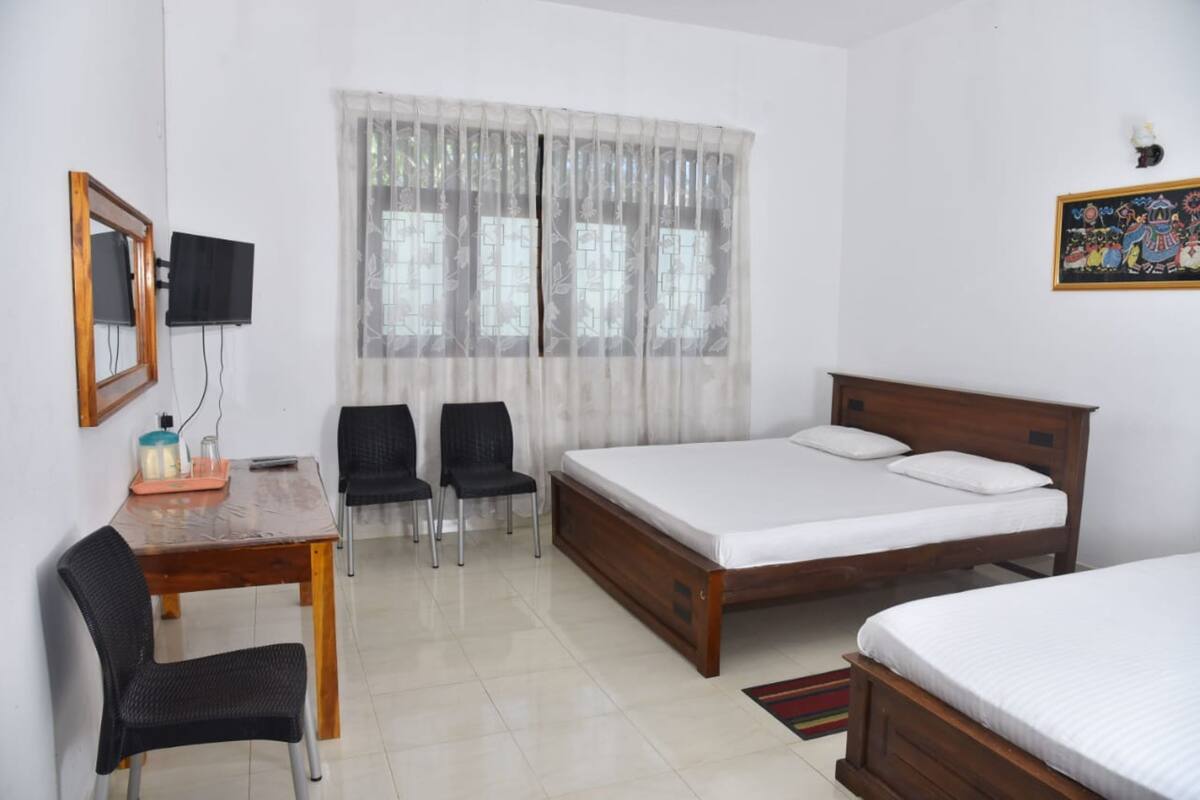 A room with a wooden bed, a desk with chairs, a television, and a window with curtains.