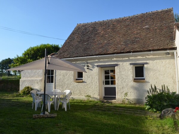 A white building with a tiled roof, a door, and windows. There is a table with chairs outside.