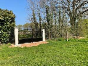 A gated entrance with a metal gate, a paved path, and a grassy area with trees.