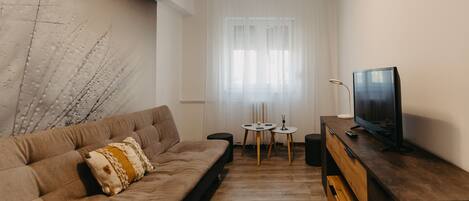 Ein modernes Wohnzimmer mit einer Couch, einem Fernseher auf einem Holzboden und einem kleinen Tisch mit Kerzen.
