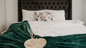 A neatly made bed with white linens, a dark headboard, and a floral pillow.