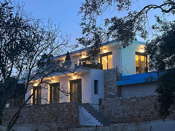 Une maison moderne à deux étages, dotée d’une façade en pierre, de grandes fenêtres et d’un escalier menant à l’étage supérieur.
