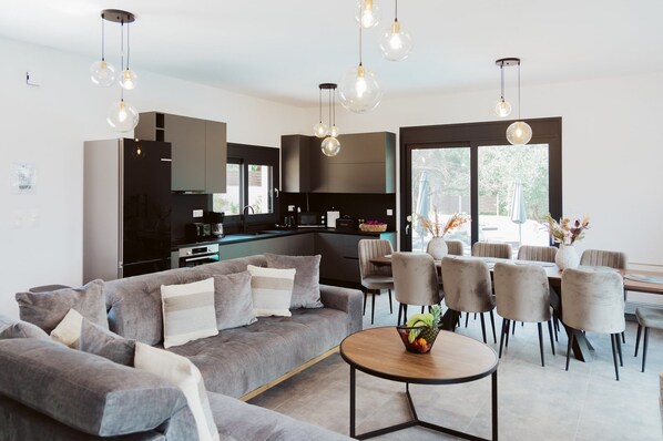A modern living room with a grey sofa, a round coffee table, and a dining area with grey chairs and a table.
