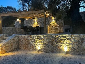Une terrasse extérieure avec des murs en pierre et une pergola en bois, agrémentée de tables et de chaises.