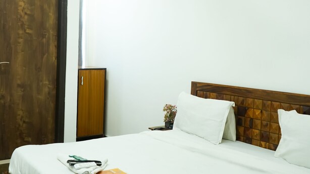 A hotel room with a bed, a ceiling fan, a wooden wardrobe, and a wall-mounted light fixture. - Roomshala 028 Blu Lagoon (New Delhi)