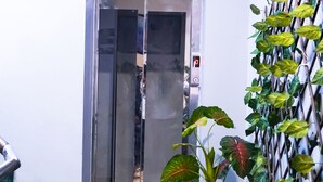 A hotel lobby with a glass elevator, a potted plant, and a wall-mounted TV. - Roomshala 028 Blu Lagoon (New Delhi)