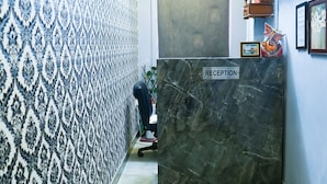 A reception area with a marble reception desk, patterned wallpaper, a ceiling fan, and a bed in the foreground. - Roomshala 028 Blu Lagoon (New Delhi)