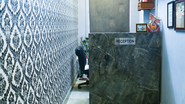 A reception area with a marble reception desk, patterned wallpaper, a ceiling fan, and a bed in the foreground. - Roomshala 028 Blu Lagoon (New Delhi)