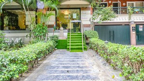 L’entrée d’un hôtel, avec un escalier menant à un espace abrité, entouré de verdure.