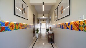 A hallway with a tiled floor, framed artwork on the walls, and a potted plant. - FabHotel VJR Electronic City (Bengaluru)