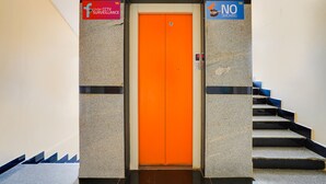 An elevator with a bright orange door, flanked by signs indicating 'Under CCTV Surveillance' and 'No Smoking'. - FabHotel VJR Electronic City (Bengaluru)