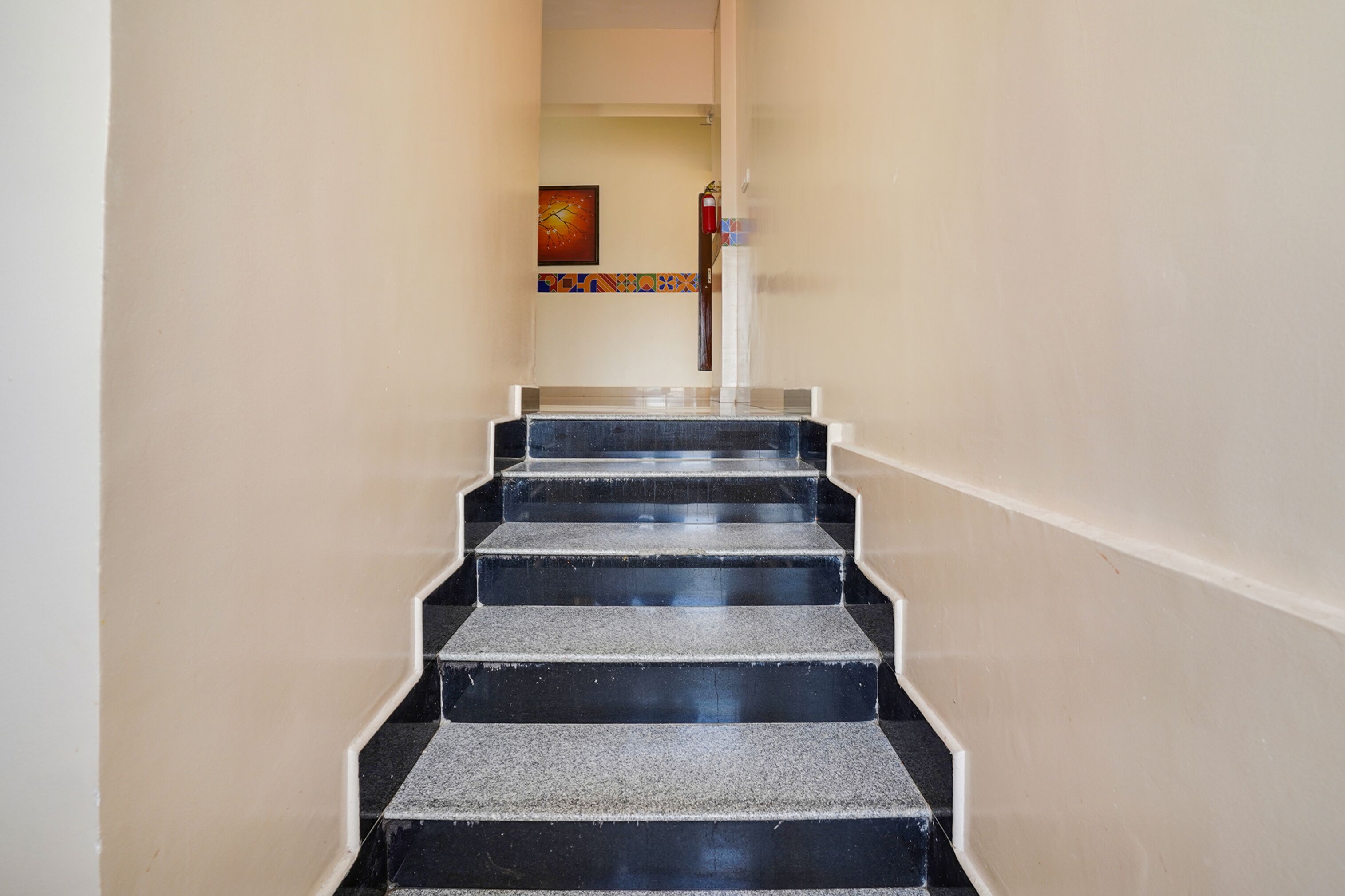 A staircase with black steps leading to a room with a door and a fire extinguisher on the wall.