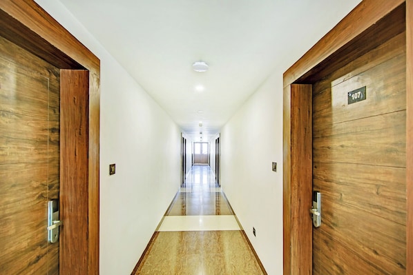 A long, narrow hallway with wooden doors on either side, leading to a bright room at the end.