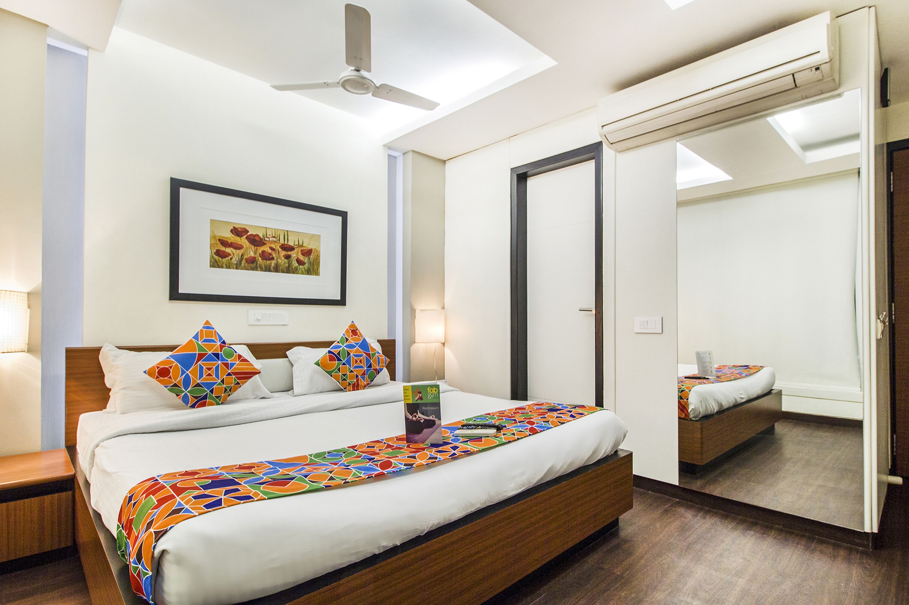 Quarto de hotel moderno com uma cama grande, um ventilador de teto, uma moldura com uma fotografia na parede e um espelho na porta.