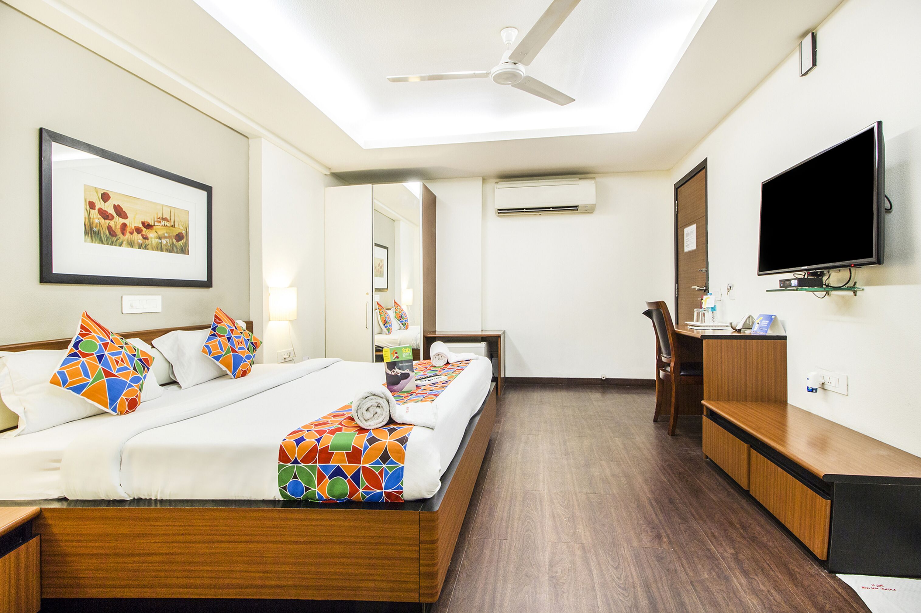 A hotel room with a bed, a desk, a television, and an air conditioning unit.