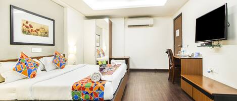 A hotel room with a bed, a desk, a television, and an air conditioning unit.