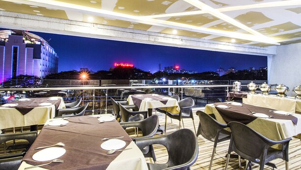 A rooftop restaurant with tables set for dining, overlooking a cityscape at night. - Fabhotel Prime Avenue (Indore)