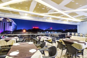 A rooftop restaurant with tables set for dining, overlooking a cityscape at night. - Fabhotel Prime Avenue (Indore)