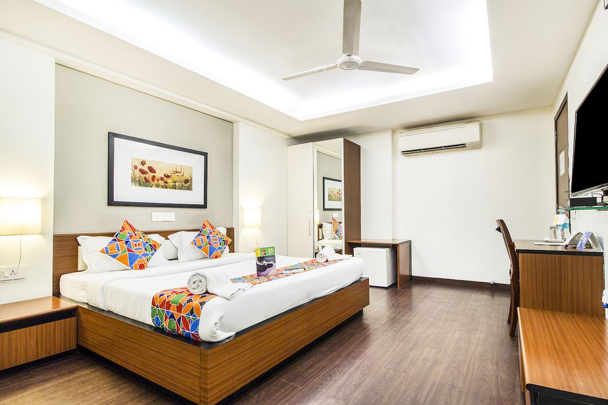 A hotel room with a bed, bedside tables, a desk, a chair, a ceiling fan, and an air conditioning unit.