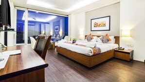 A hotel room with a bed, bedside tables, a desk, a chair, a television, and a large window. - Fabhotel Prime Avenue (Indore)