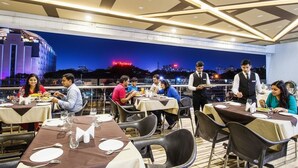 An outdoor dining area with tables set for guests, a waiter attending to a table, and a cityscape view in the background. - Fabhotel Prime Avenue (Indore)